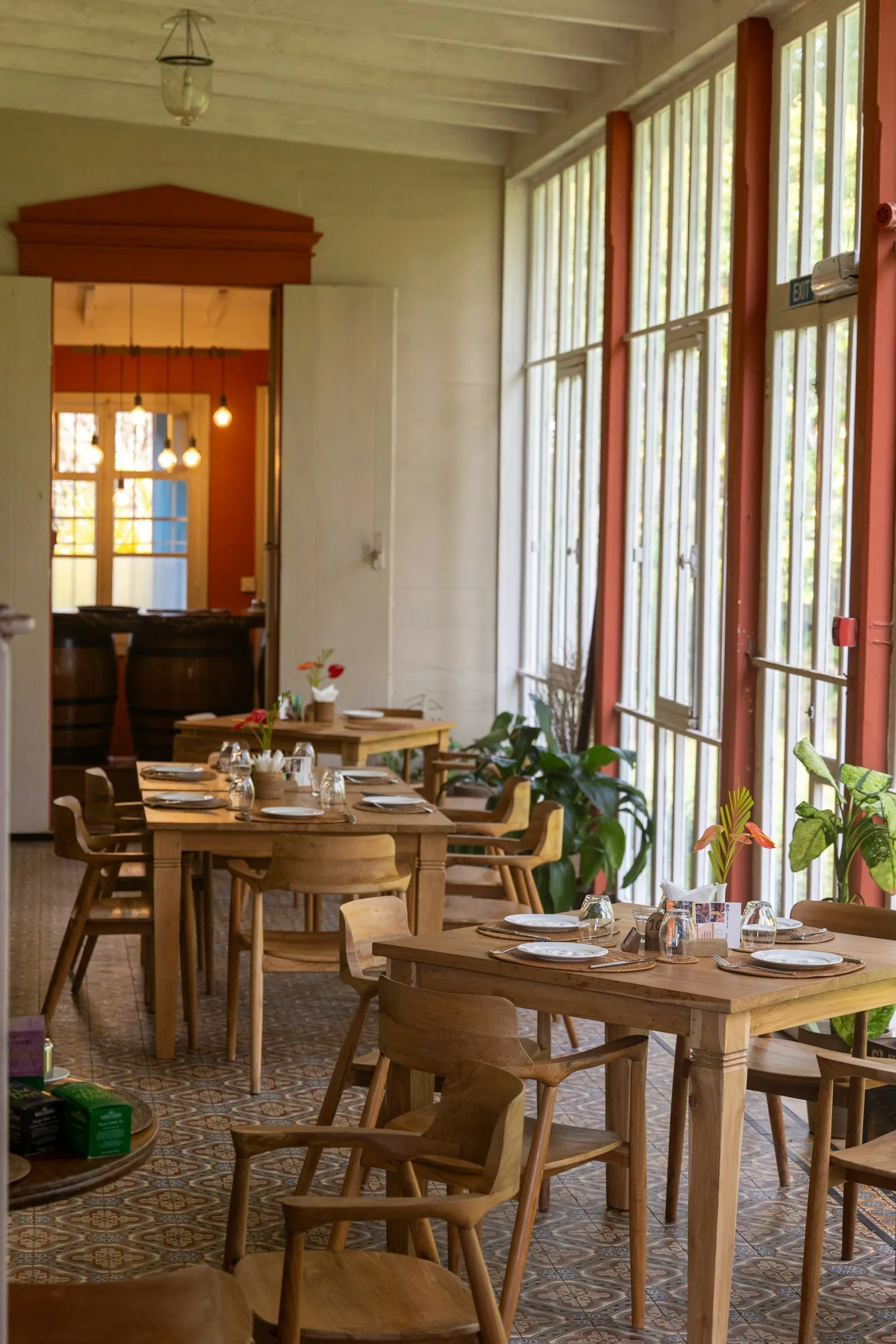 El salón de un restaurante con mesas de madera preparadas para el servicio, luz natural y piso de baldosa hidráulica.
